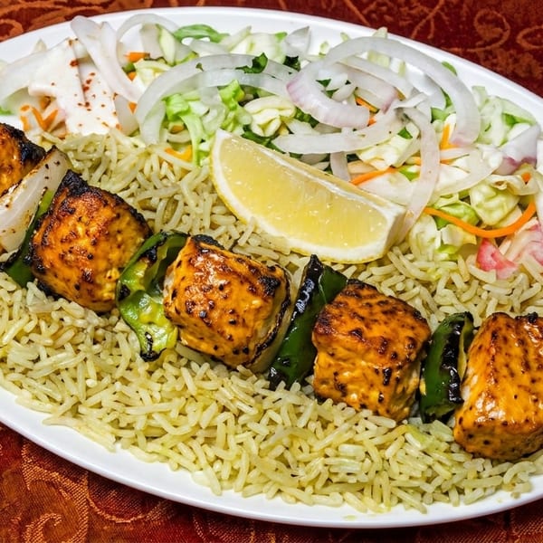 Chicken tikka skewer with rice, salad, and a lemon wedge on a white plate.