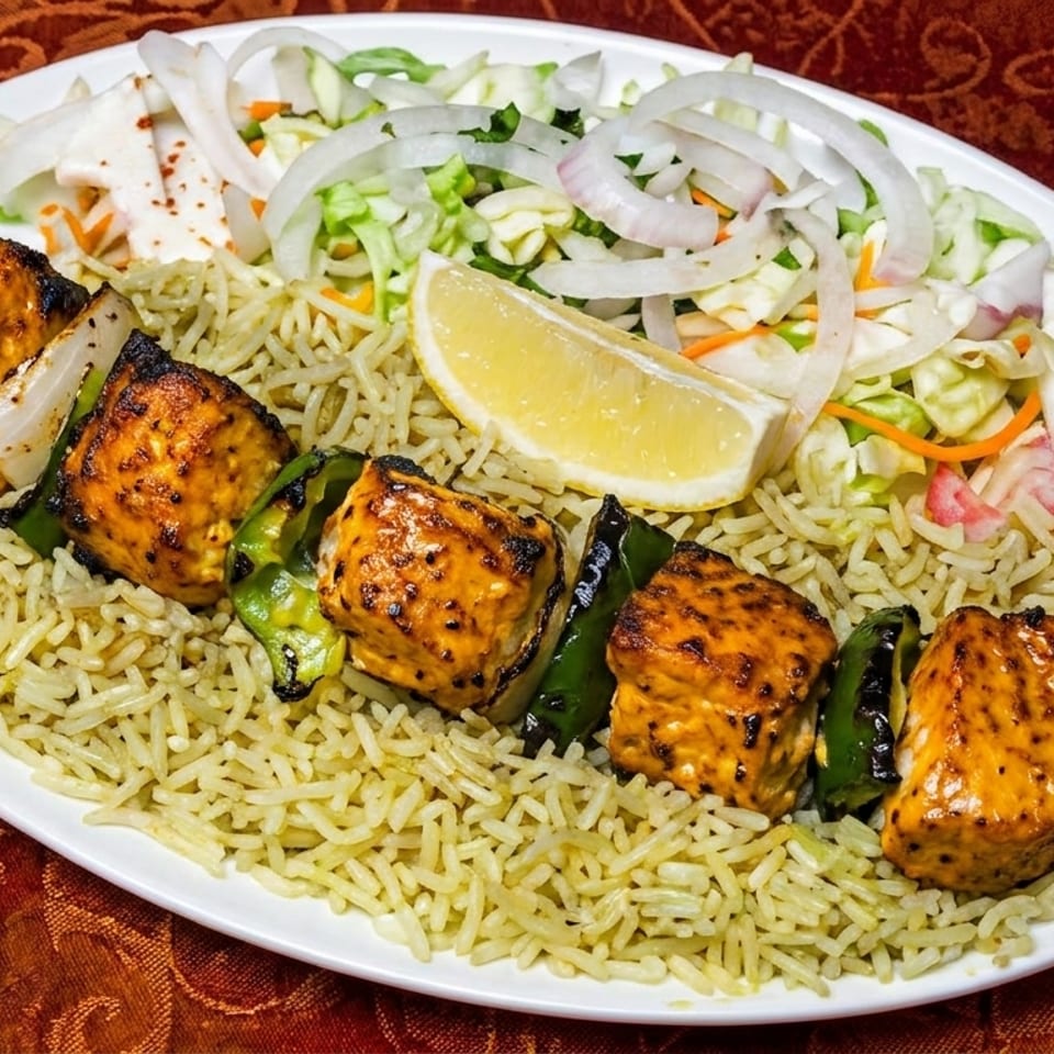 Chicken tikka skewer with rice, salad, and a lemon wedge on a white plate.