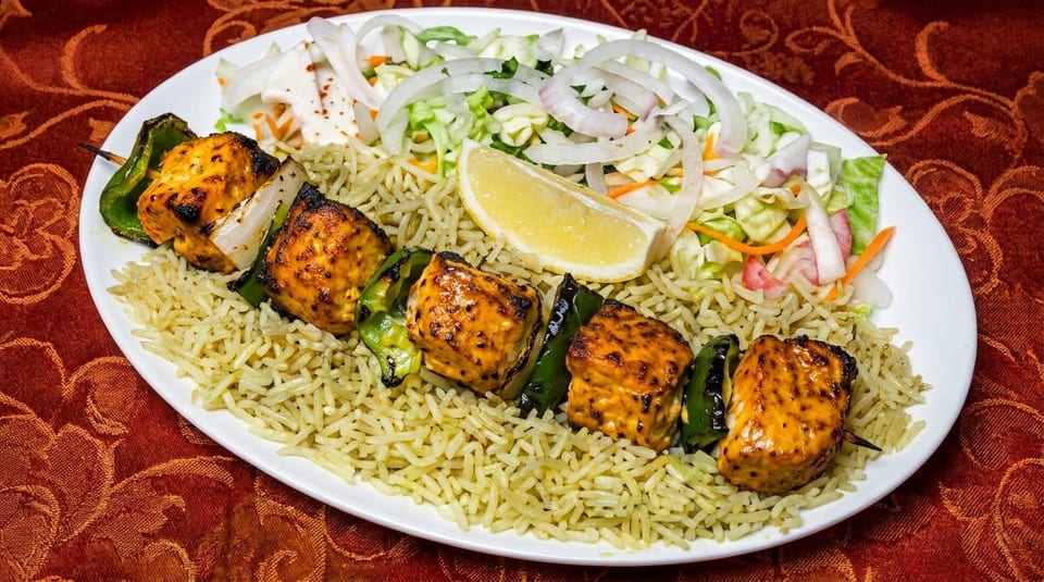 Chicken tikka skewer with rice, salad, and a lemon wedge on a white plate.