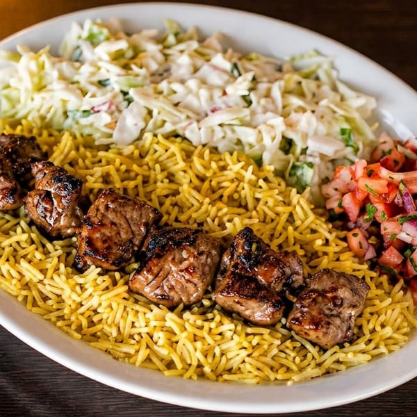 Grilled meat skewers on yellow rice with coleslaw and tomato salsa on a white plate.
