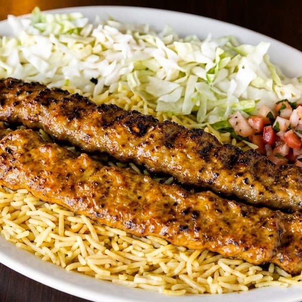 Two grilled meat skewers on a bed of rice, with shredded cabbage and tomato salsa.