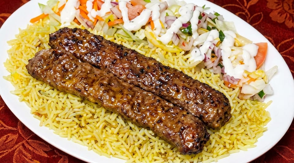 Two glistening grilled kebabs on a bed of yellow rice with a side salad and white sauce.